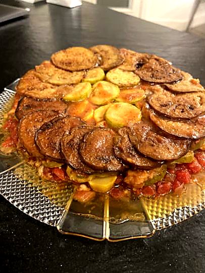 Ratatouille arranged in concentric rings of eggplant, squash, and tomato on a glass dish.